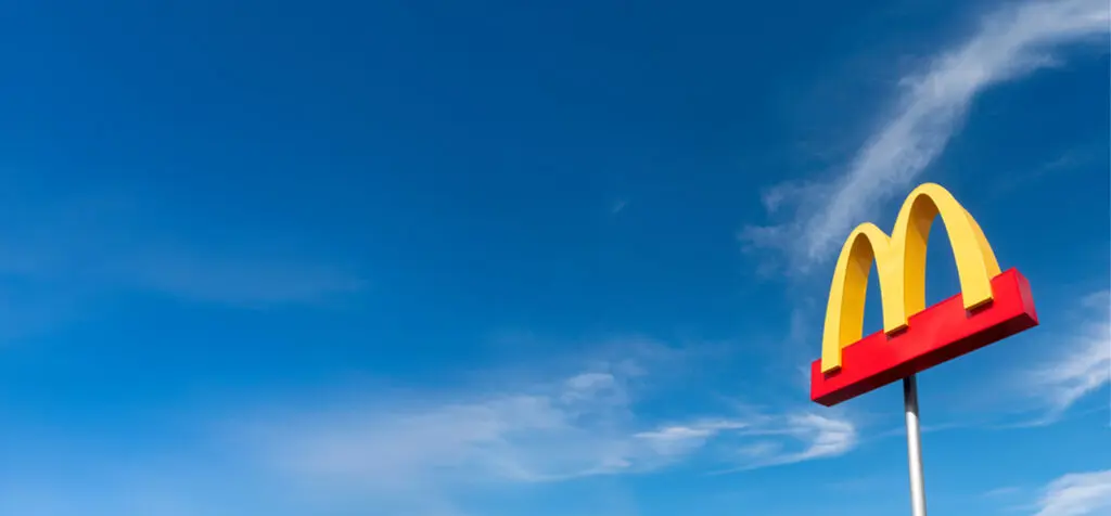 Ein gelbes McDonald's-Schild auf einem hohen Mast steht vor einem strahlend blauen Himmel mit ein paar Wolkenfetzen.