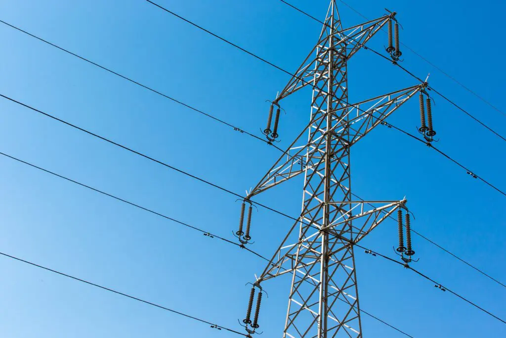 Ein hoher metallener Hochspannungsmast mit mehreren Stromleitungen ragt in den klaren blauen Himmel.